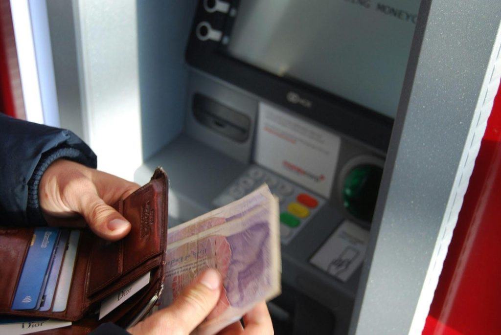 person holding cash in front of an ATM - featured image